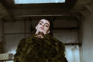 Portrait of a person wearing a textured dark green fringe garment inside an industrial space