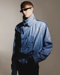 Model wearing a blue leather jacket and dark sunglasses against a plain neutral background for the COLORS project.