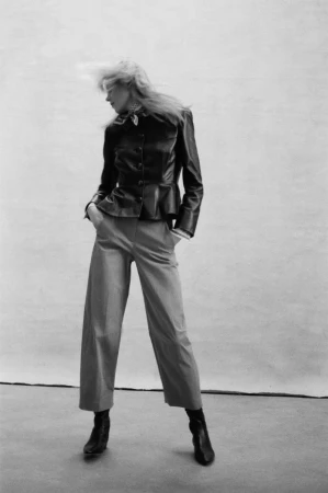 Model with motion-blurred blonde hair wearing a dark leather jacket and trousers against a neutral studio backdrop