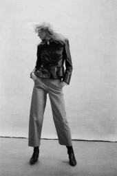 Model with motion-blurred blonde hair wearing a dark leather jacket and trousers against a neutral studio backdrop