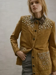 Model wearing a tan crystal-embellished suede jacket and grey trousers against a light grey studio background