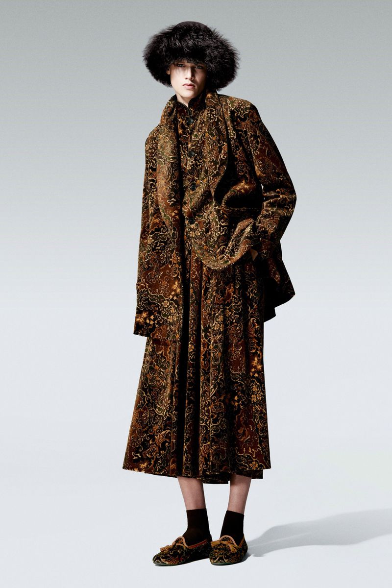 A single adult wearing a brown patterned jacket, skirt, and hat posing in a full shot against a white background in a studio.