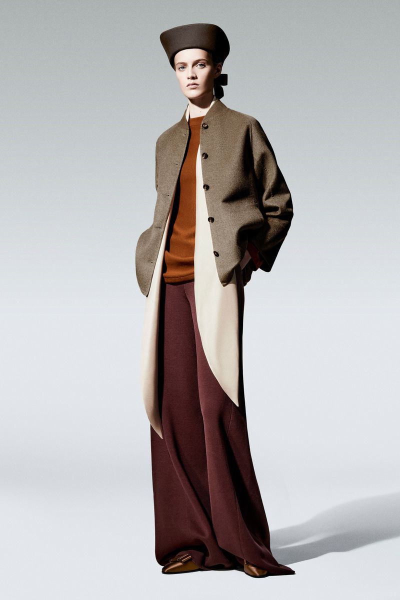 Elegant studio shot of a fashion model in a brown jacket, rust-colored top, maroon pants, and a brown hat, set against a neutral backdrop.