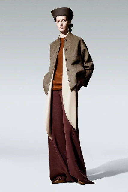 Elegant studio shot of a fashion model in a brown jacket, rust-colored top, maroon pants, and a brown hat, set against a neutral backdrop.