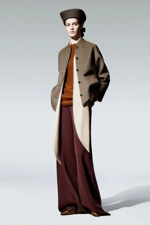 Elegant studio shot of a fashion model in a brown jacket, rust-colored top, maroon pants, and a brown hat, set against a neutral backdrop.