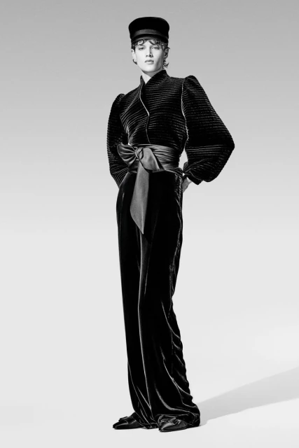 A black and white studio shot of a woman in an elegant black velvet outfit consisting of a top with a ribbon and wide pants.