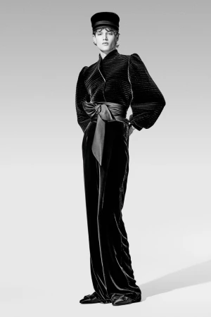 A black and white studio shot of a woman in an elegant black velvet outfit consisting of a top with a ribbon and wide pants.