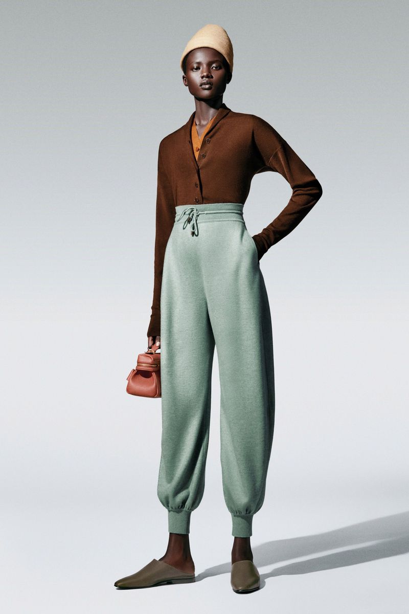 Fashionable adult woman posing in studio wearing a brown long-sleeve cardigan, light green pants, and a beige headscarf.