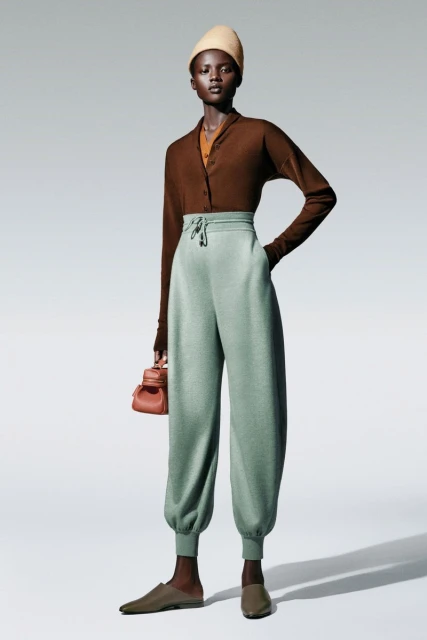 Fashionable adult woman posing in studio wearing a brown long-sleeve cardigan, light green pants, and a beige headscarf.
