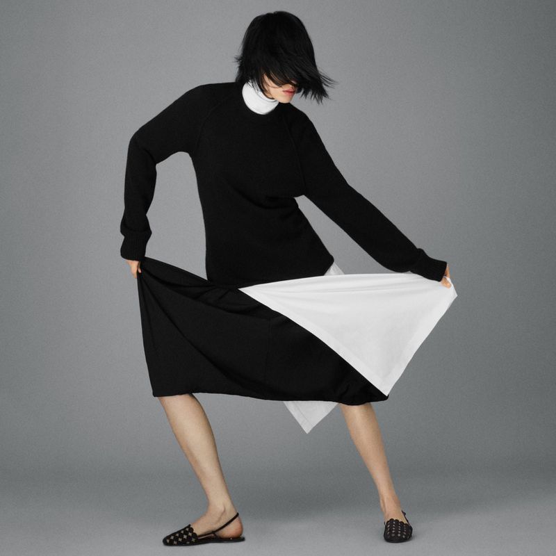 Fashion shoot of a woman in a black and white dress and black flats against a gray background in a photo studio. Minimalist style.