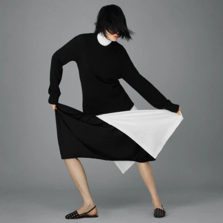 Fashion shoot of a woman in a black and white dress and black flats against a gray background in a photo studio. Minimalist style.