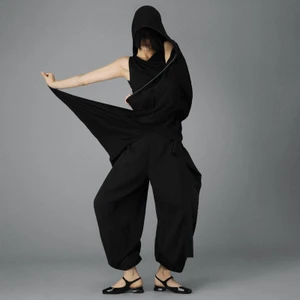 Model in black hooded outfit and strapped flats posing against grey seamless studio background