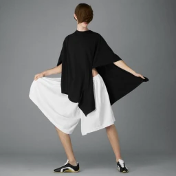 Model in black top and white shorts holding garment edges against grey seamless background