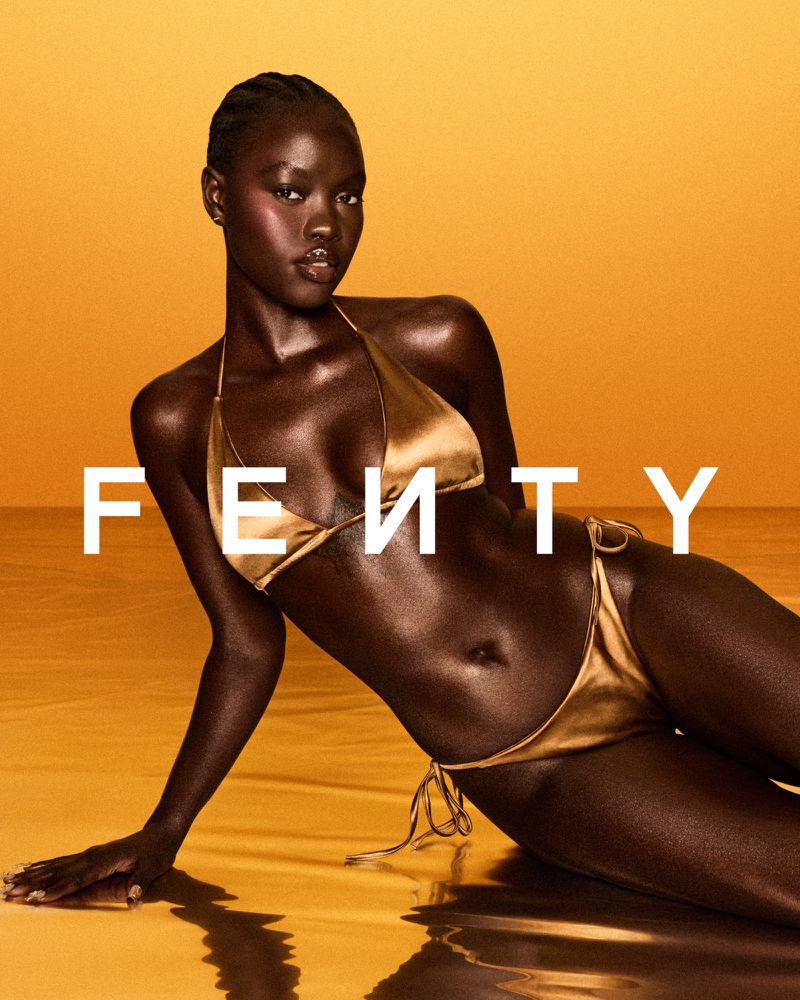 Woman poses in gold bikini against yellow background for Fenty Beauty advertisement, promoting makeup and swimwear products.