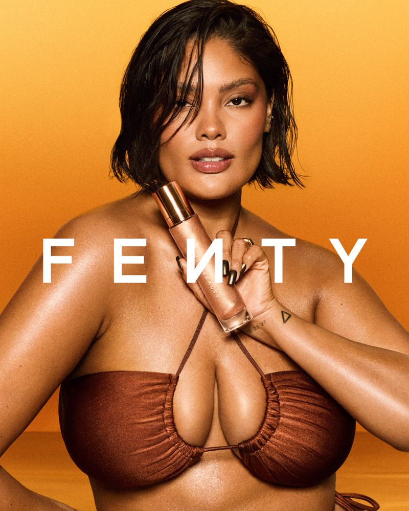A woman poses against an orange gradient background, holding Fenty product. She wears brown bikini top, with her short hair styled to the side.
