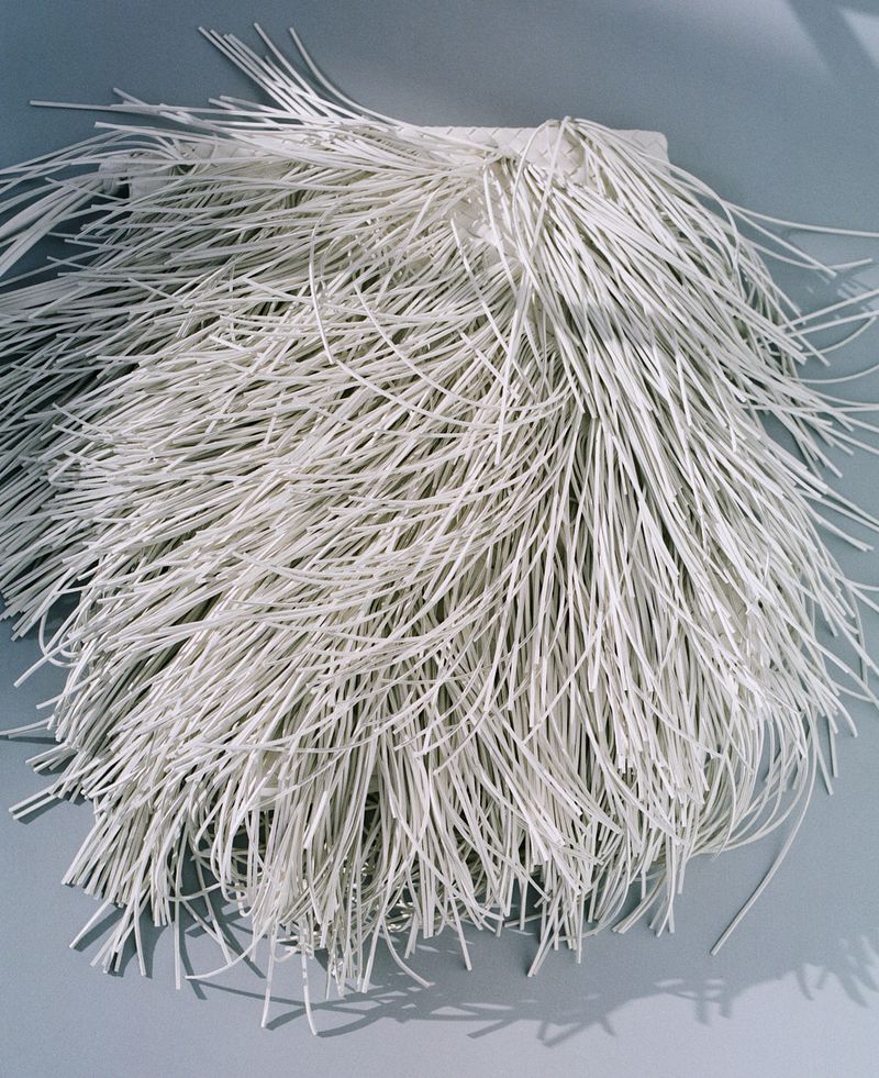 Abstract arrangement of thin, white, straw-like objects fanning out, with a shallow depth of field, on a pale grey surface, studio lighting.
