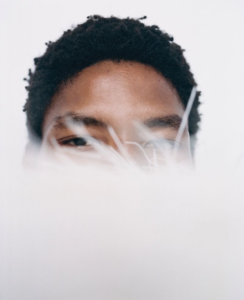 Close-up portrait of an adult, light-skinned person with dark hair partially obscured by white fluffy material against a white backdrop.