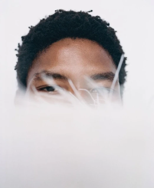 Close-up portrait of an adult, light-skinned person with dark hair partially obscured by white fluffy material against a white backdrop.