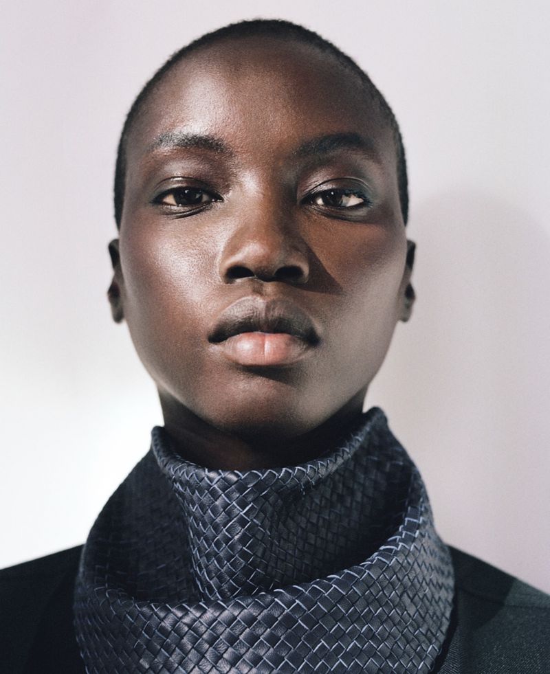 Close-up portrait of an African female with smooth skin, wearing a textured scarf and dark jacket against a bright white background.
