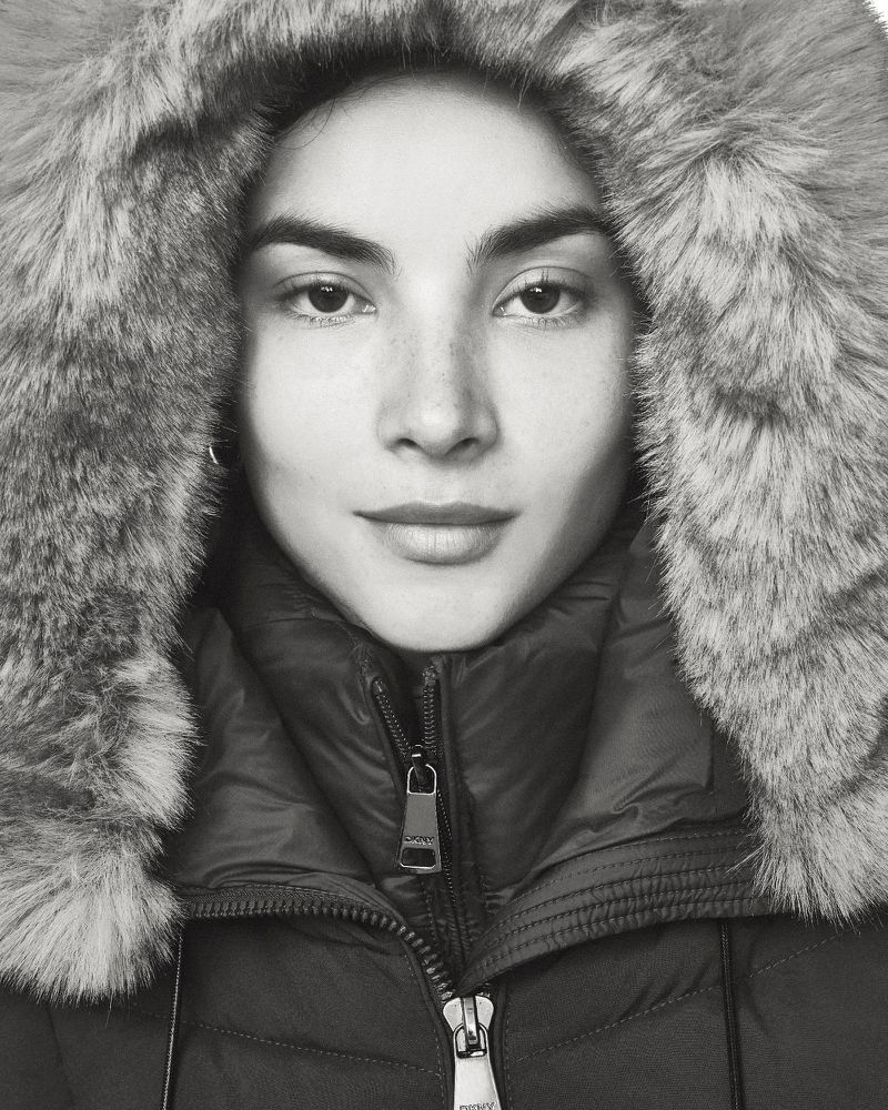 Close-up of a woman with fair skin wearing a fur-trimmed parka jacket, looking directly at the camera in a studio setting.