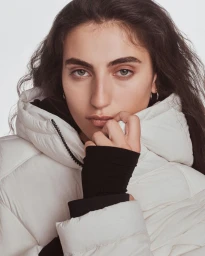 Close-up portrait of a model wearing a white puffer jacket with a black inner layer against a seamless backdrop