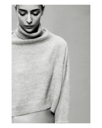 Monochrome portrait of a woman with short dark hair looking down, wearing a light grey wool turtleneck sweater on a grey background.