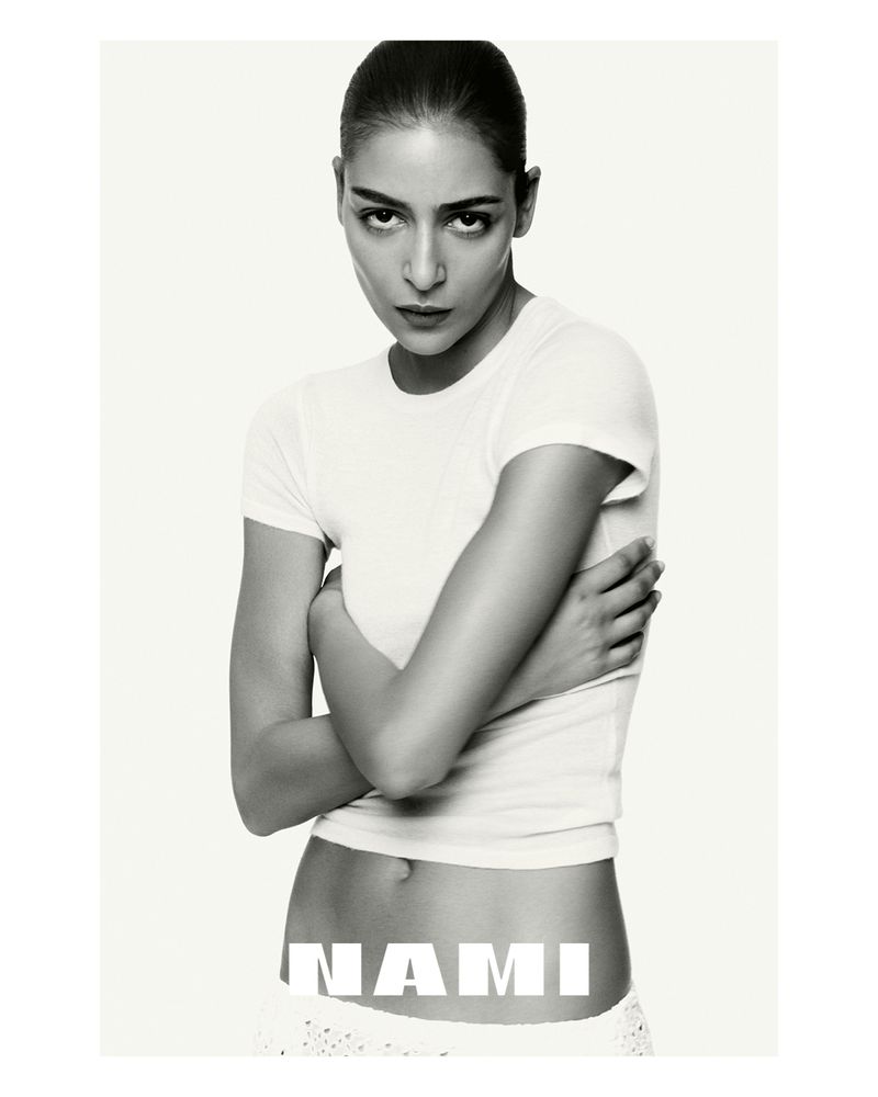 Monochrome portrait of a female model in a white t-shirt with crossed arms and neutral expression, against a plain white backdrop with text.