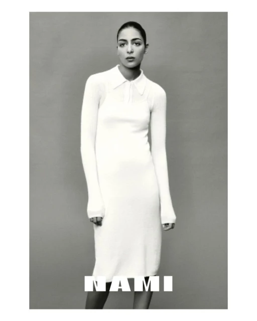Monochrome shot of a woman posing indoors wearing a long-sleeve, collared dress. The text 'NAMI' is overlaid on the lower portion of the image.