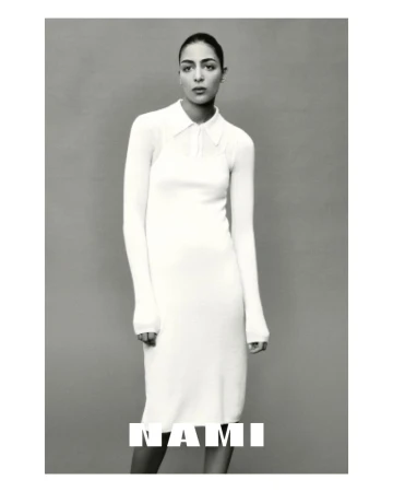 Monochrome shot of a woman posing indoors wearing a long-sleeve, collared dress. The text 'NAMI' is overlaid on the lower portion of the image.