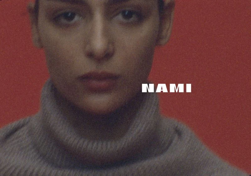 Close-up studio portrait of a young adult female with fair skin wearing a gray turtleneck sweater against a red background.
