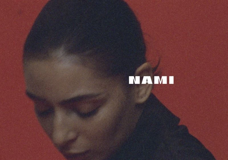 Close-up studio shot of a young adult woman with dark hair against a red background, featuring the white text overlay 'NAMI'.