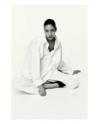 Model Nora Attal in an oversized white shirt and trousers sitting on a plain white floor for Nami fashion campaign.