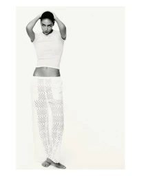 Model Nora Attal posing against a white seamless backdrop wearing a white t-shirt and patterned trousers for Nami Drop 4.