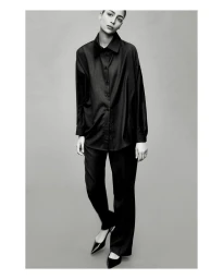 Monochrome portrait of model Nora Attal wearing a dark button-down shirt and trousers against a grey studio backdrop.