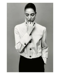 Model Nora Attal wearing a high-collared light jacket against a neutral grey studio background