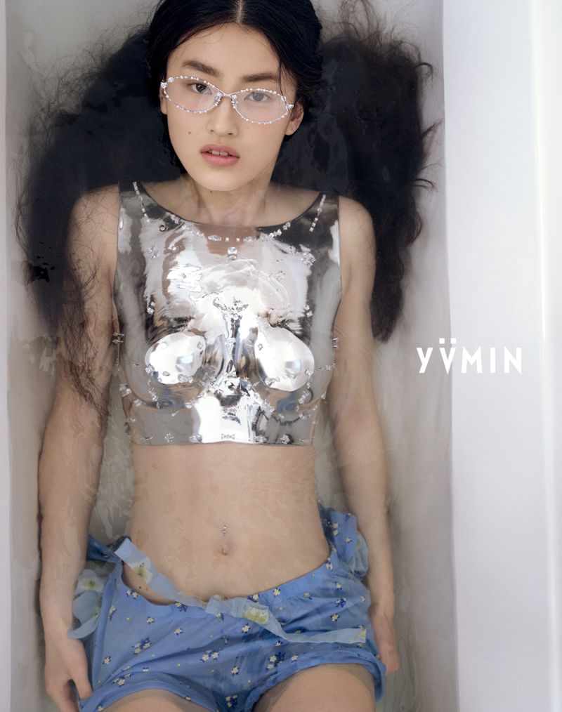 Asian woman in water with reflective silver top and glasses. Long black hair spread around her. Shot from overhead in indoor setting.