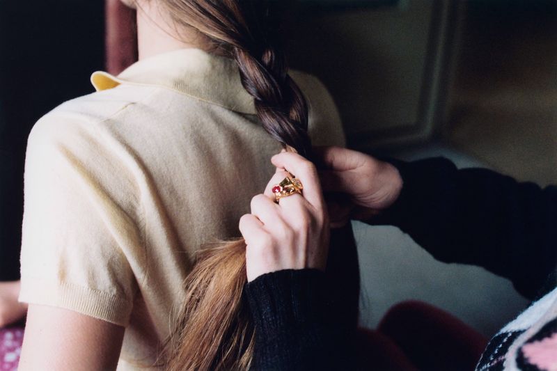 Blonde woman with a braid is being styled indoors. The photo showcases a close-up of the styling process and the subject's yellow top.
