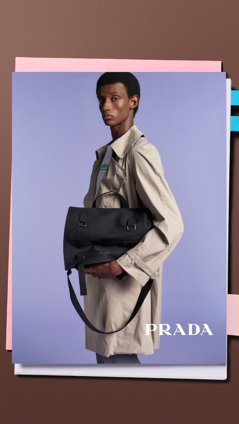 A person holds a Prada bag in a studio shot, showcasing a stylish trench coat and a sleek, professional aesthetic with a clean backdrop.