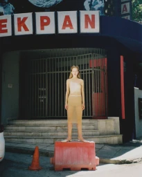 Model standing on a red plastic barrier in front of a dark building with white and red signage for Cake Magazine project DOWN AND OUT.