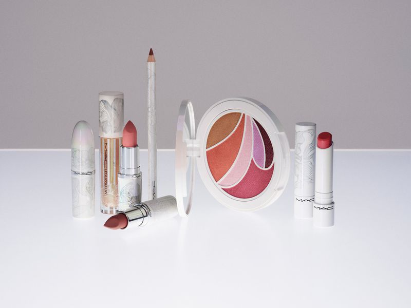 Close-up still life of MAC makeup products including lipsticks, lip pencil, and blush palette, all with light pink, white, and coral tones.
