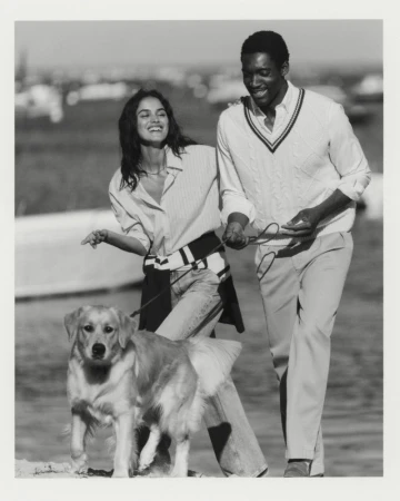 Black and white editorial photo of a smiling woman and man walking a golden retriever outdoors for Gant