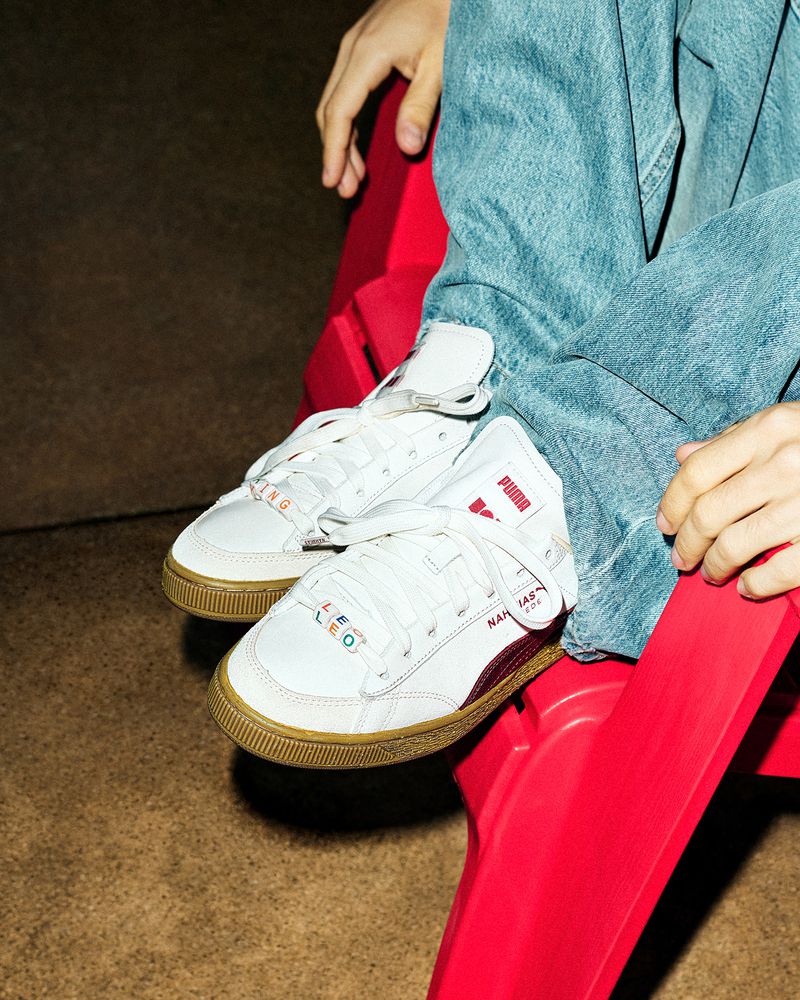 Close-up of a seated person wearing jeans and white Puma sneakers with a red chair, focusing on fashion and footwear.