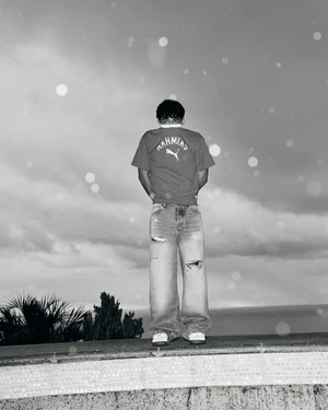 Monochrome portrait of Charles Leclerc wearing a graphic t-shirt and distressed denim jeans against an open sky backdrop.