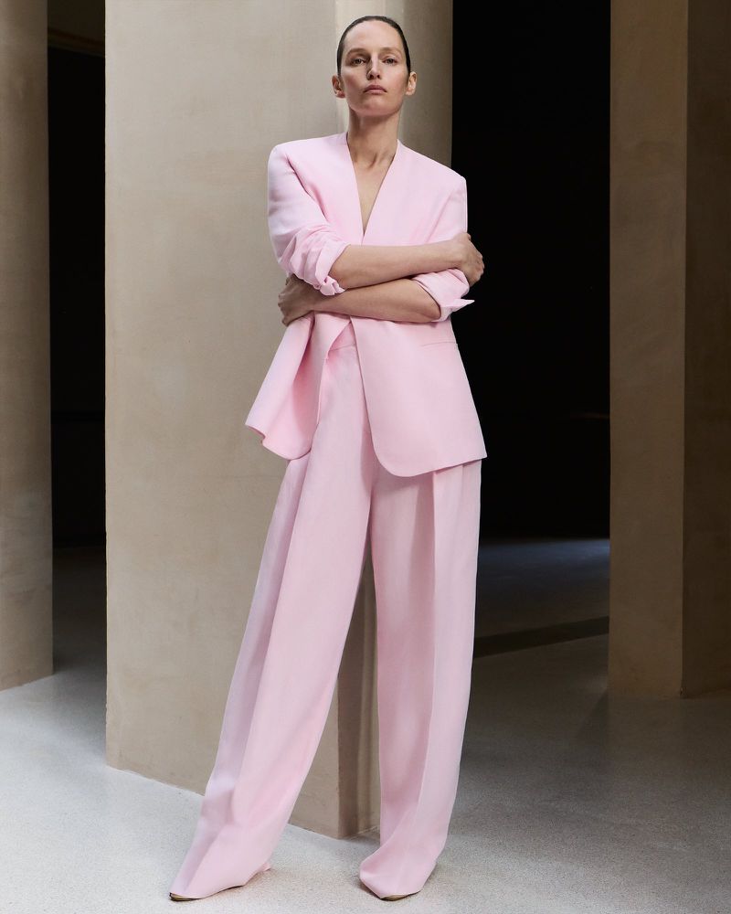 Fashion-forward woman in a light pink suit poses indoors, showcasing a modern and elegant style with neutral background.