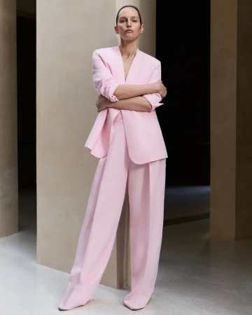 Model Vivien Solari in a pink blazer and matching trousers leaning against a neutral pillar for Fabiana Filippi