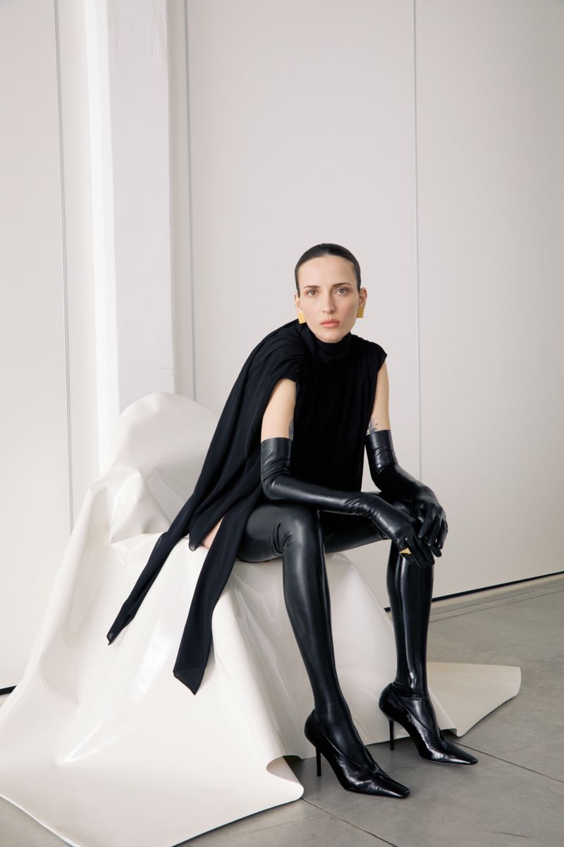 Elegant woman in black top and thigh-high boots poses indoors. Stylish studio portrait for fashion or beauty concept.