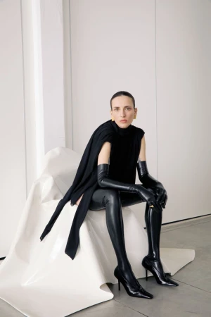 Elegant woman in black top and thigh-high boots poses indoors. Stylish studio portrait for fashion or beauty concept.