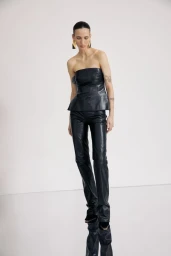 Model wearing a black leather strapless top and matching trousers against a minimalist white studio background.