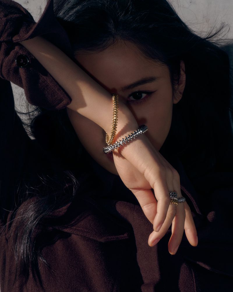 Close-up studio shot of a fashionable Asian woman with dark hair wearing a brown jacket and jewelry consisting of a bracelet and ring.