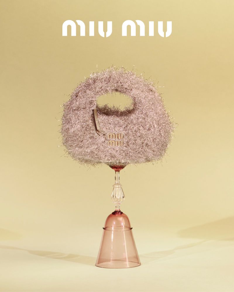 Elegant Miu Miu handbag displayed on a stemmed wine glass, set against a soft yellow backdrop, showcasing luxury fashion.